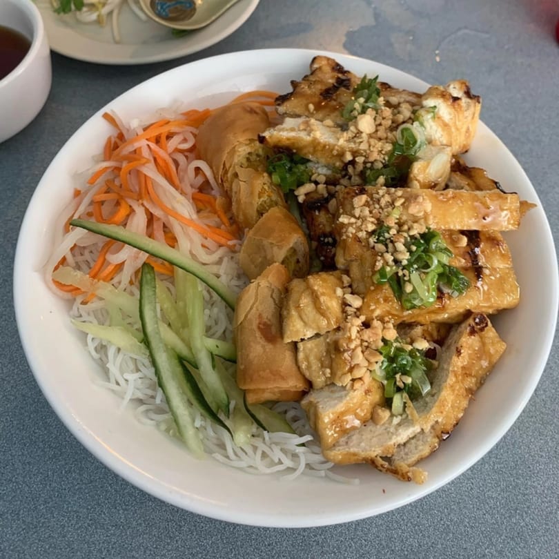 Vietnamese vermicelli bowl with grilled pork, spring rolls, pickled carrots, cucumber, and crushed peanuts.