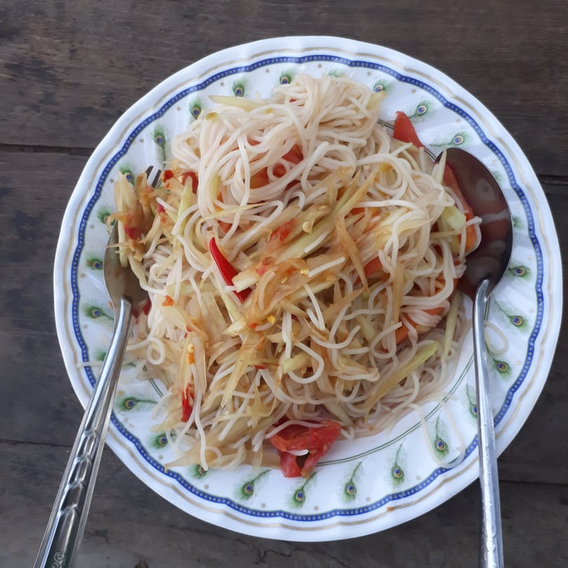 Vietnamese papaya salad with rice vermicelli noodles, tomatoes, and chili on a peacock-patterned plate.