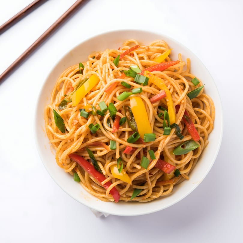 A white bowl of Vietnamese stir-fried noodles with red and yellow bell peppers and green onions.