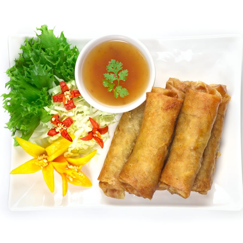 Crispy Vietnamese spring rolls with sweet chili dipping sauce, lettuce, and chili garnishes on a white plate.